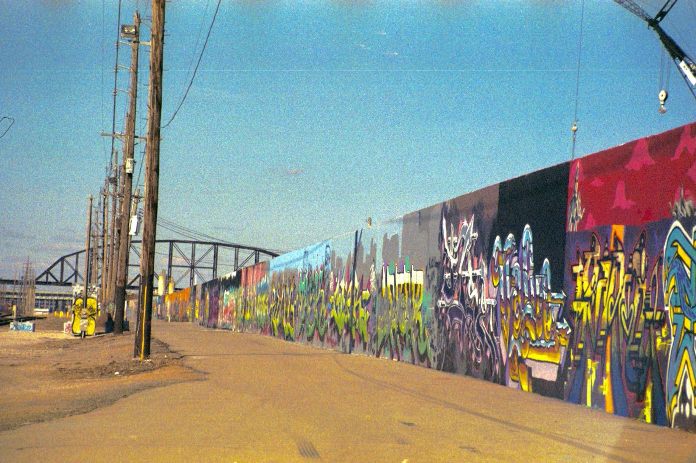 A photograph of a grafitti wall with a bridge in the background.