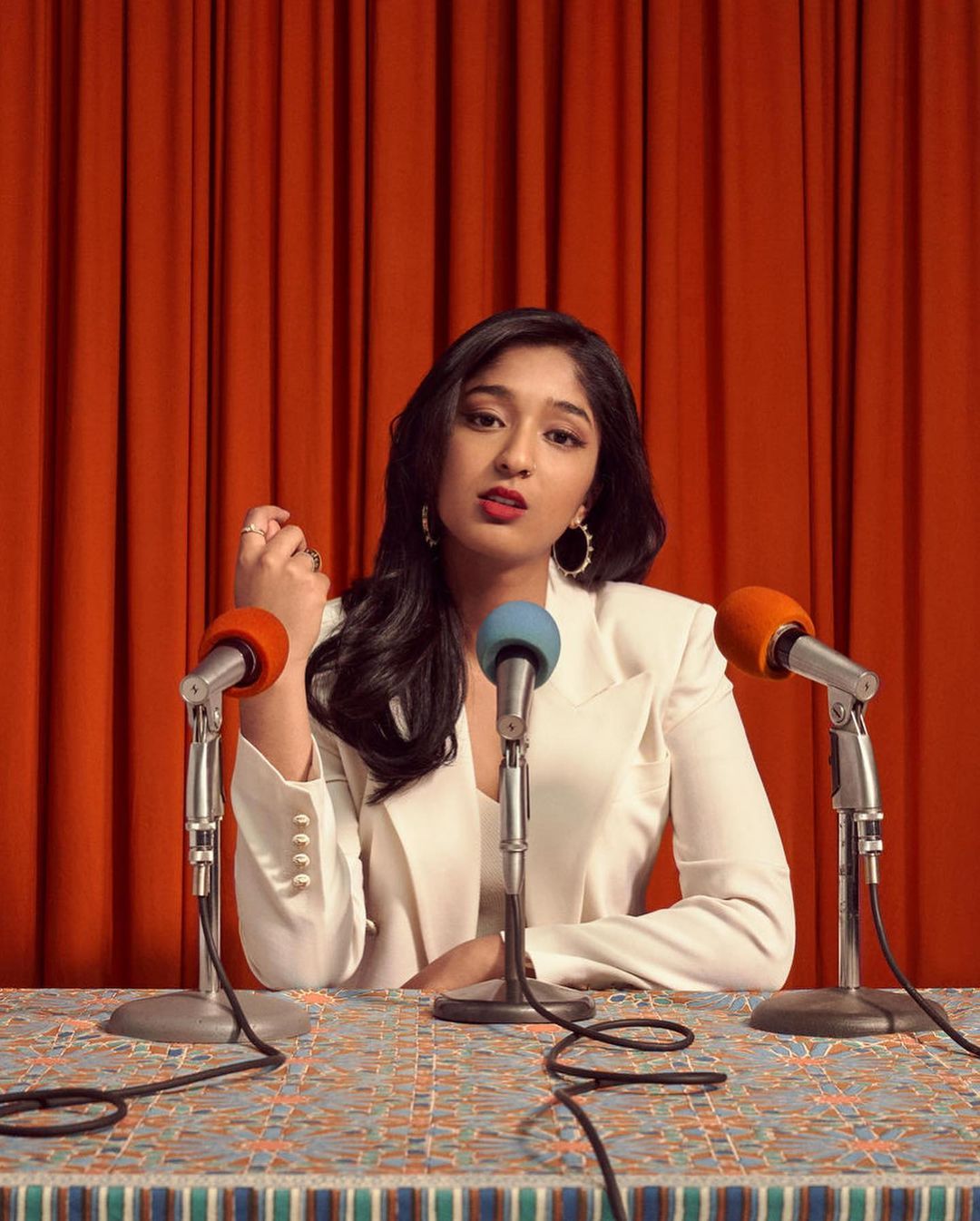 Picture of Indian woman wearing white suit with 3 microphones pointed towards her.