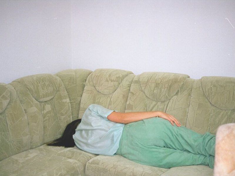 A photograph of a woman lying down on a green couch, facing away from the camera.